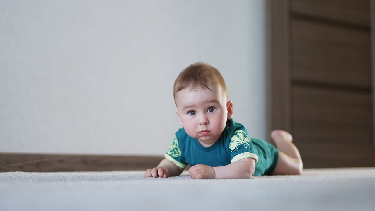Amazing lovely kid lies still on the floor looking surprised. Nice boy starts to bang his hands and legs by the floor actively.