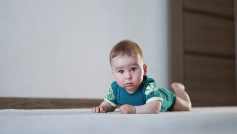 amazing lovely kid lies still on the floor looking surprised. nice boy starts to bang his hands and legs by the floor actively.