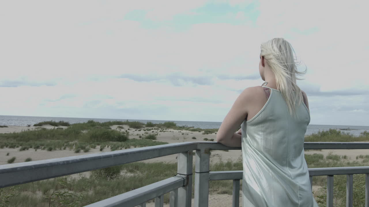 Rear shot of blond girl looking at wide sea during windy day in summer,slow motion