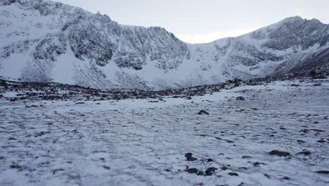 Aerial-drone-footage-slowly-rising-towards-the-Mountain-Stob-Coire-an-t-Sneachda-in-the-Cairngorms-National-Park-of-Scotland-in-snow,-ice-and-full-winter-mountaineering-conditions-with-clear-blue-sky