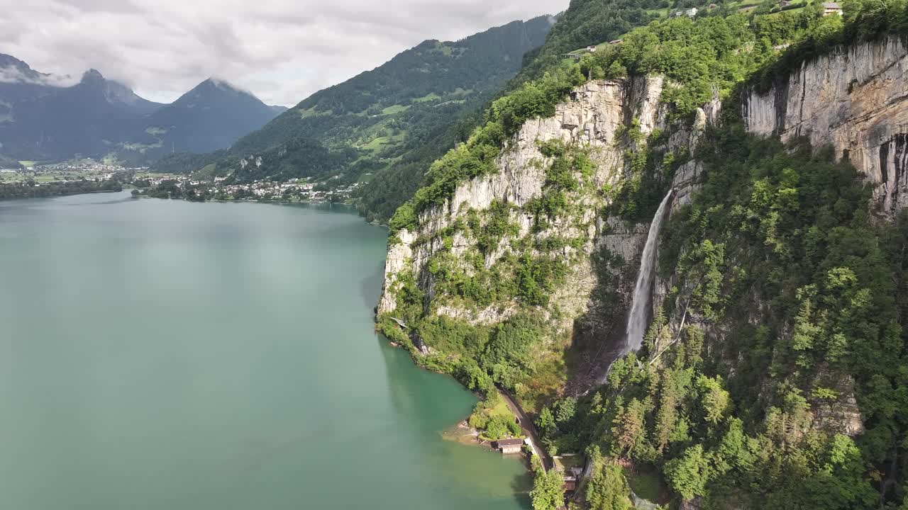 Scenic aerial view of Seerenbach Falls cascading down cliffs into Lake Walensee near Betlis, Switzerland, framed by lush green mountains and turquoise waters