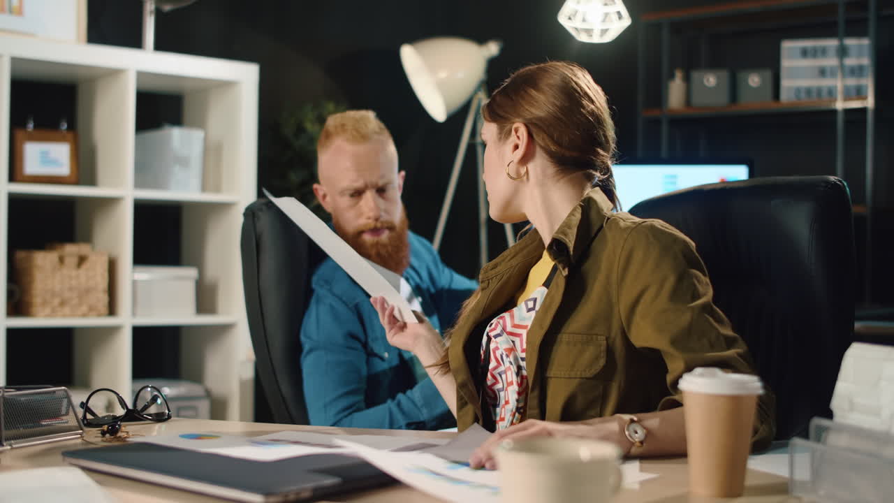 Seriøs mand og hipsterpige diskuterer arbejdsdokumenter på et moderne kontor.