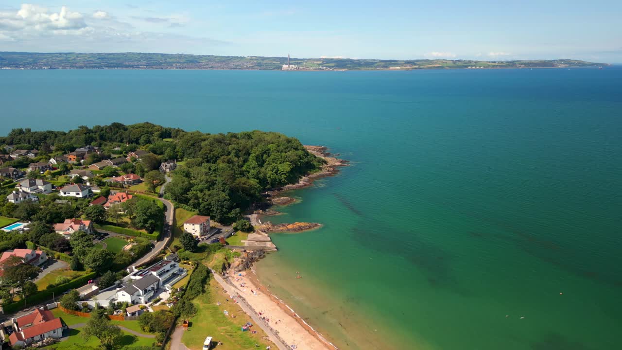 Video aereo invertito della foresta e del mare blu presso la spiaggia di Helen's Bay, nella Contea di Down, Irlanda del Nord, Regno Unito, in una luminosa giornata estiva. Filmato in 4K, 60FPS e con colore Rec709.