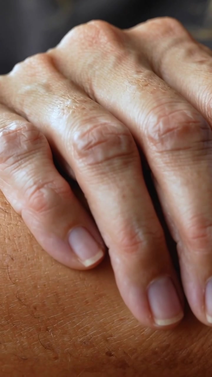Video verticale: Mano adulta che si posa, facendo sottili movimenti delle dita su pelle abbronzata, mostrando unghie corte