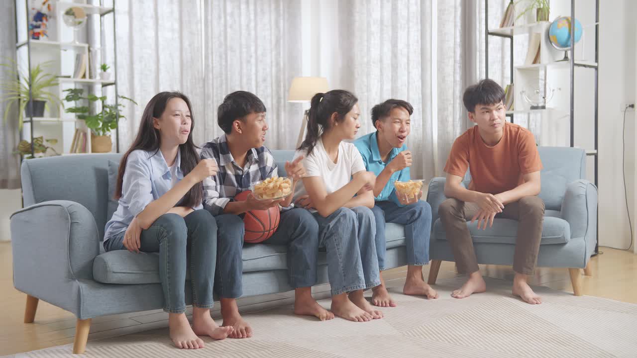 아시아 십대 들 이 집 에서 농구 경기 를 보고, 먹고, 응원 하고 있다