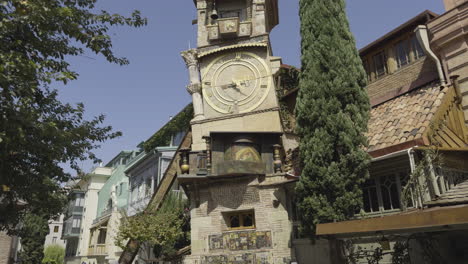 tourists walk past tbilisi’s famous leaning clock tower, capturing the city’s rich history and culture