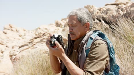 Happy-senior-biracial-man-in-mountains-taking-photos,-in-slow-motion