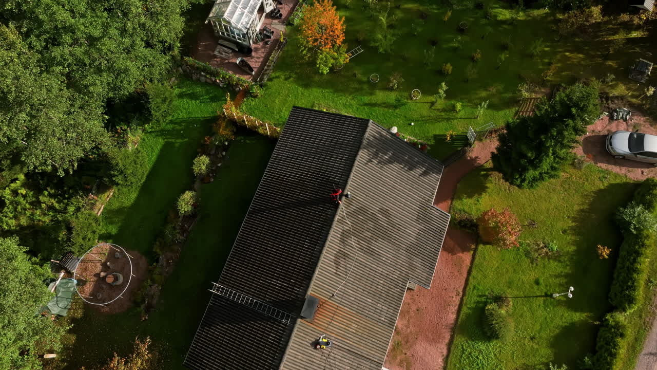 High angle drone shot of a woman pressure washing a house roof, sunny, fall day