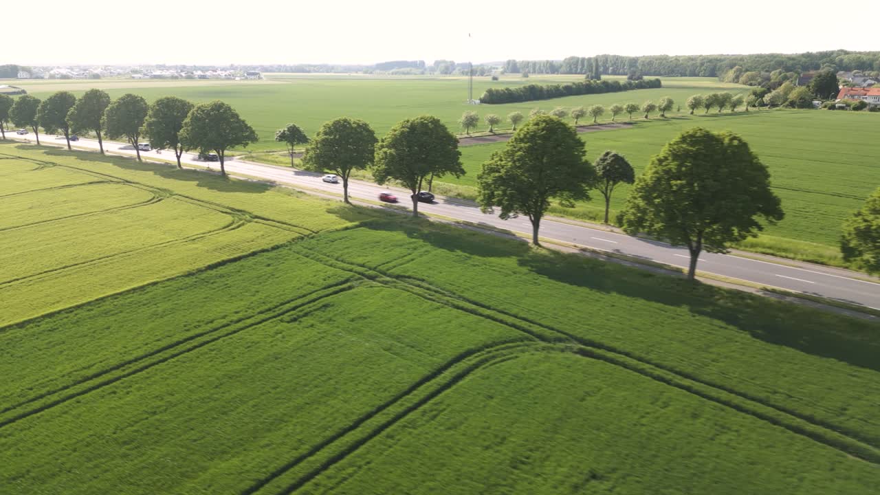 Aerial drone shot flying high over a roads passing through green farmlands in Brunswick, Germany on a sunny day