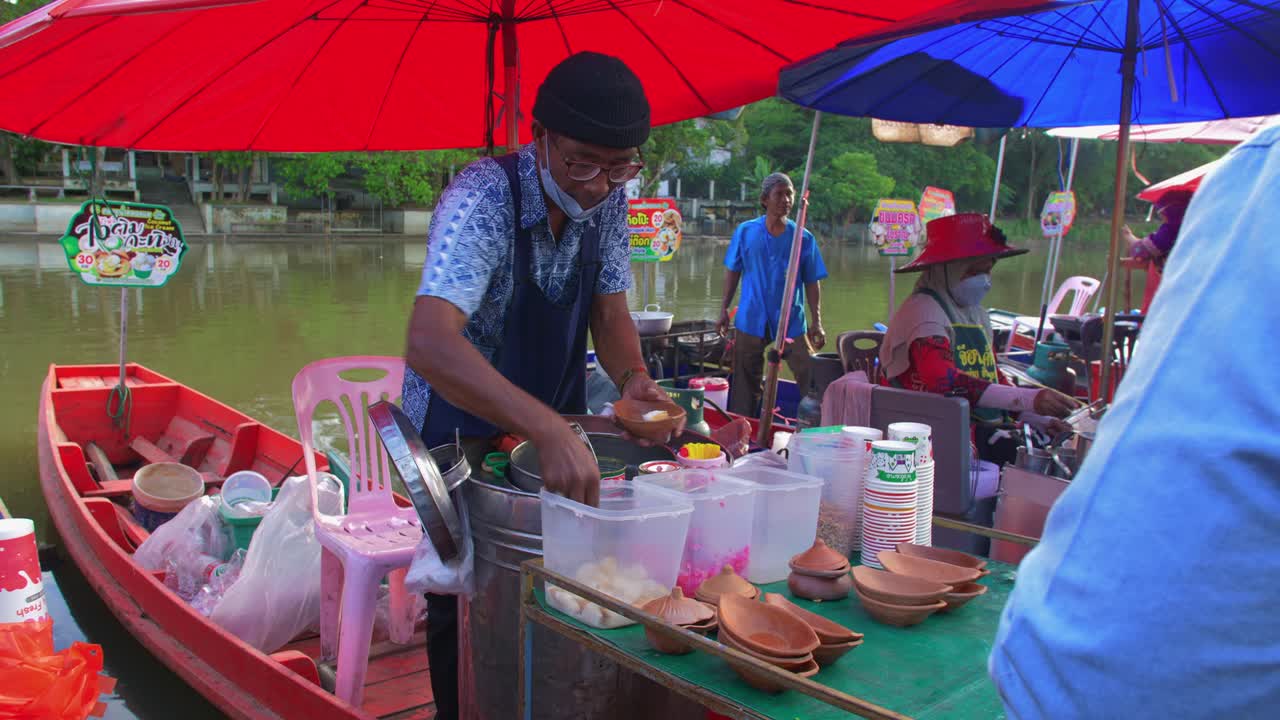 viejo hombre tailandés local que vende comida callejera asiática típica en los bancos del mercado flotante de klong hae