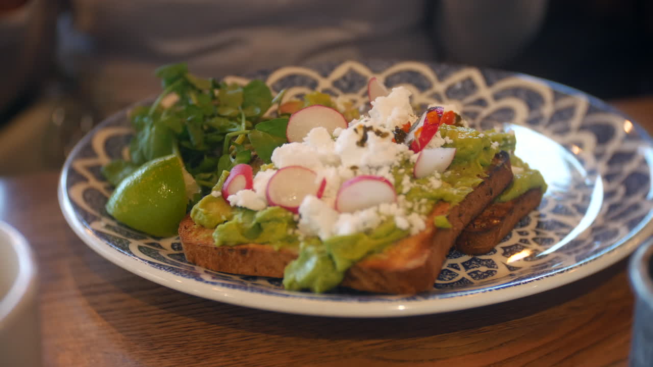 Avocado toast guarnito con ravanelli, feta ed erbe aromatiche su un piatto decorato in un caffè rustico, perfetto per colazioni salutari, turismo del benessere e branding di uno stile di vita da brunch di lusso.