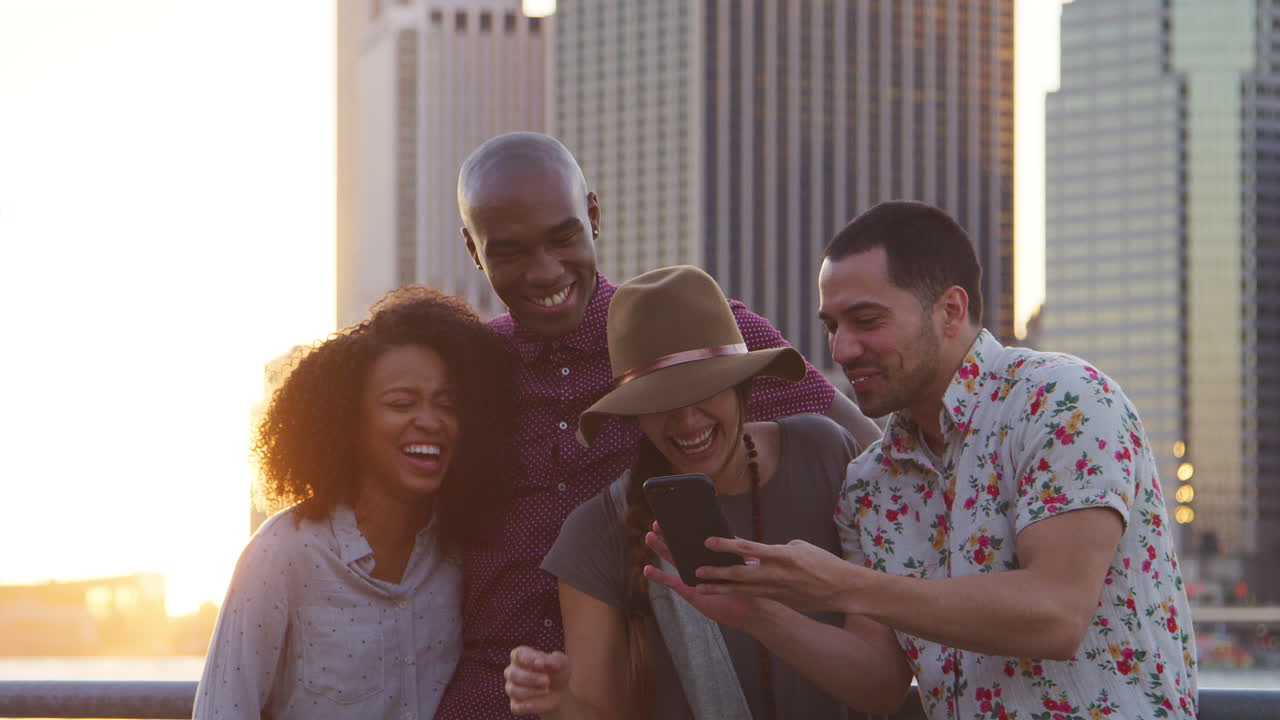 amigos miran fotos en el teléfono por el horizonte de manhattan al atardecer