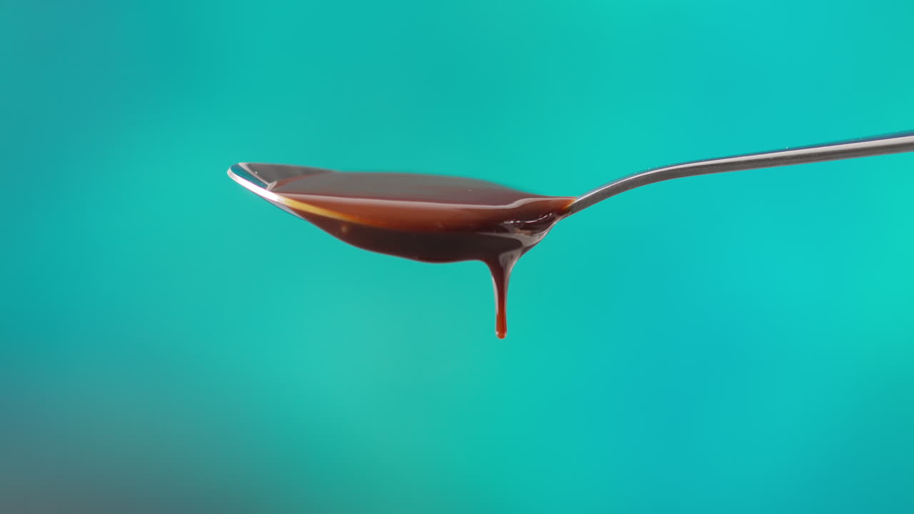 Close Up Of Melted Chocolate Dripping From Overflowing Spoon Against Blue Coloured Background With Copy Space 1