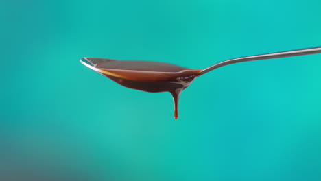 close up of melted chocolate dripping from overflowing spoon against blue coloured background with copy space 1