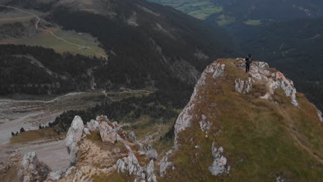 aerial shot from drone revealing young male model standing on the edge of a rock overlooking the dolomite valleys from above, italy