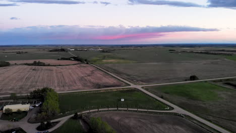 Aerial-view-of-a-countryside-agricultural-green-fields-with-road-intersection-on-a-pink-sunset