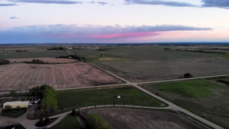 Vista-Aérea-De-Un-Campo-Verde-Agrícola-Con-Intersección-De-Carreteras-En-Una-Puesta-De-Sol-Rosa