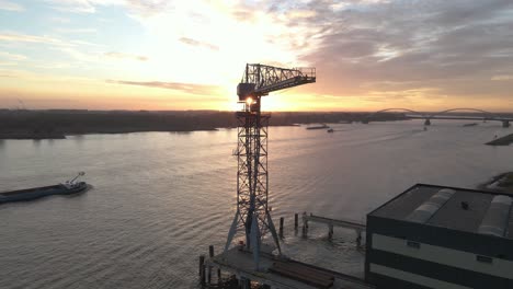 aerial sunset view of a small container terminal crane with cargo ships passing in the background