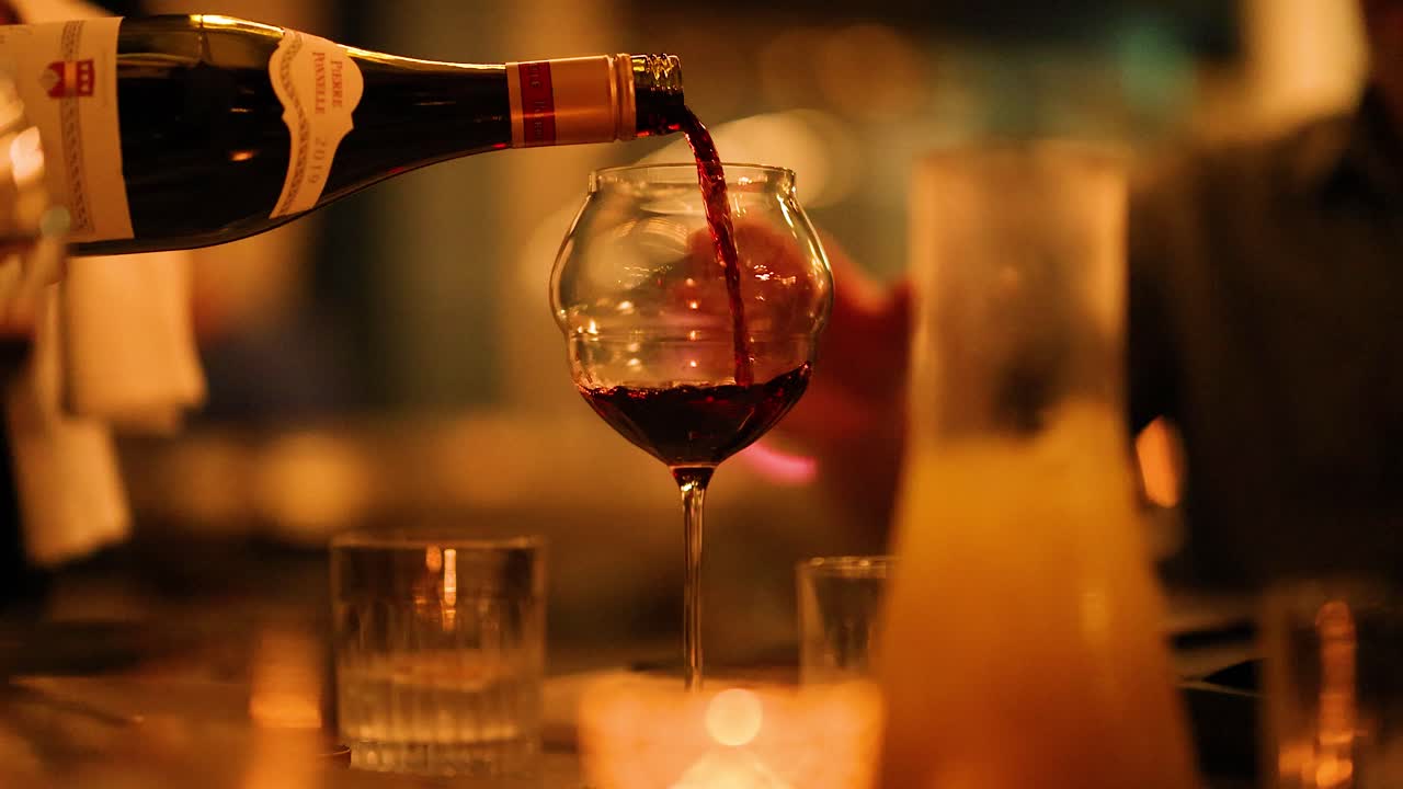 Una bottiglia di vino viene versata con grazia in un bicchiere in un ambiente caldo e illuminato a lume di candela, creando un'atmosfera sofisticata.