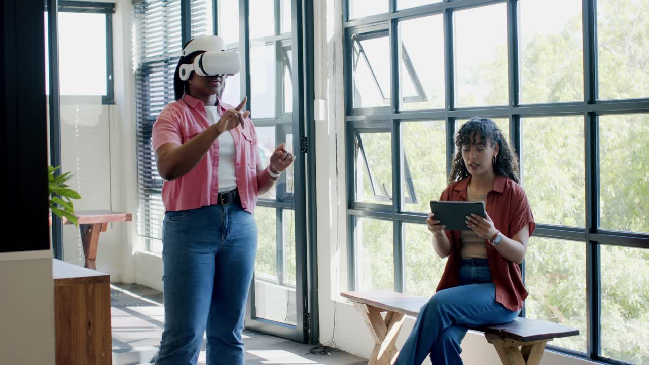 African American female team testing VR headset in studio, demo gesturing while helper using tablet