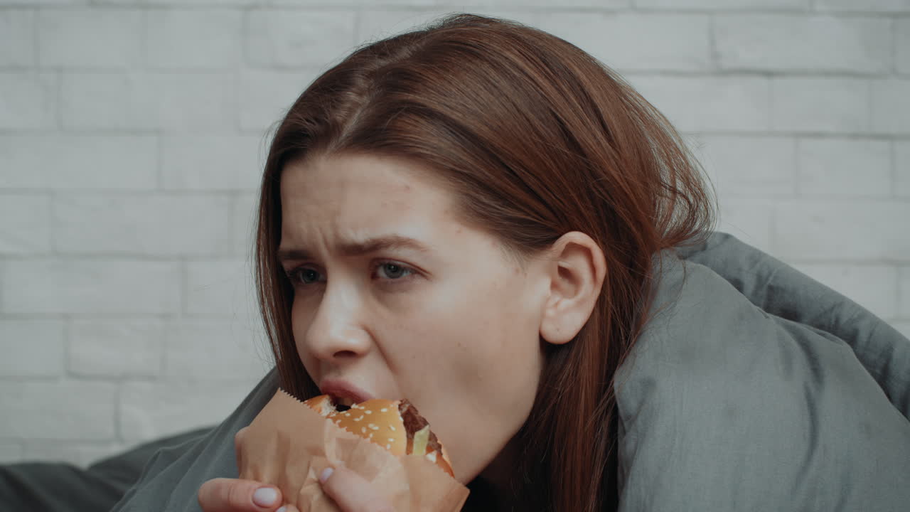 Woman eating a hamburger in bed