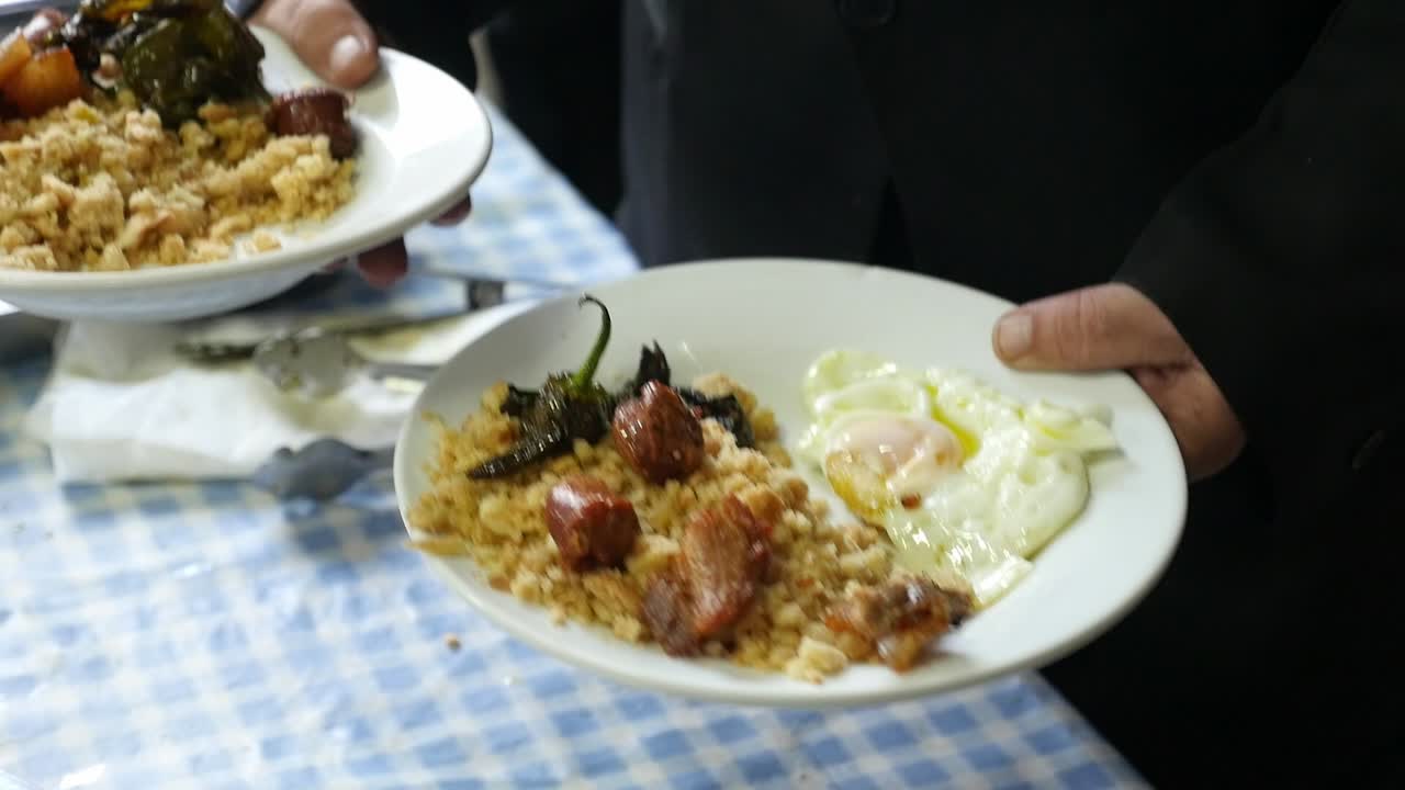 Primo piano di un cameriere che tiene due piatti di tradizionali migas spagnole con uova fritte, peperoni e chorizo.