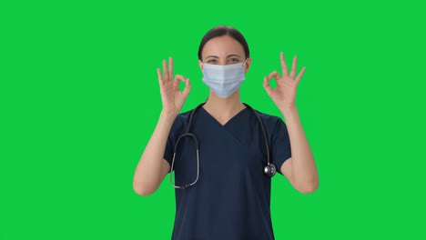 doctora india feliz mostrando un letrero de acuerdo con una máscara en la pantalla verde