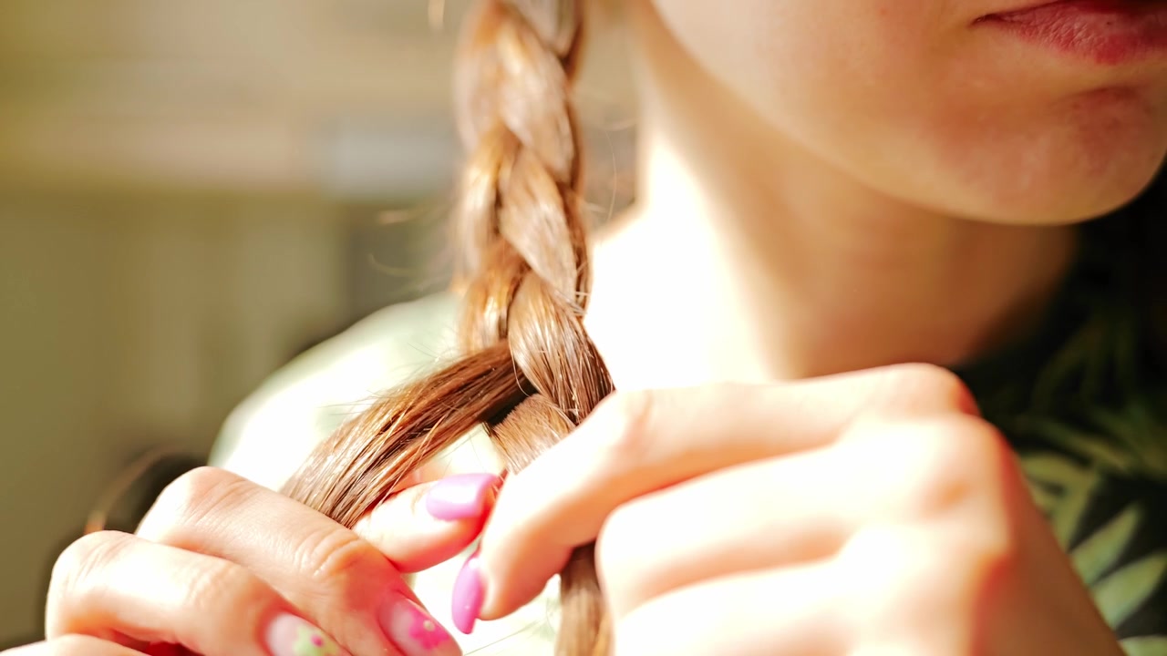 Una morbida luce solare illumina una donna che intreccia sani capelli castani al rallentatore