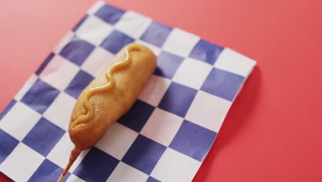 video of corn dog with mustard on a red surface