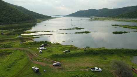 imágenes aéreas que revelan una escena de aventura al aire libre en la que camiones y autos estacionados en el lago, gente pescando, picnic, paisajes fantásticos y lagos que reflejan nubes y puesta de sol en tailandia
