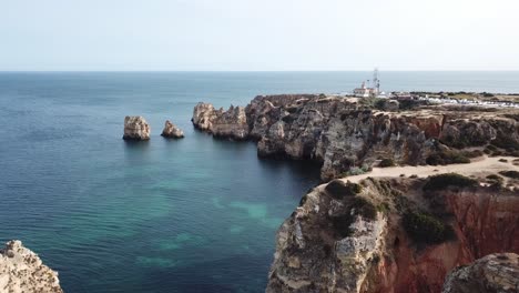 Reversing-from-Ponta-da-Piedade-lighthouse-to-reveal-Algarve-sea-cliffs-and-coast-near-Lagos,-Portugal,-aerial