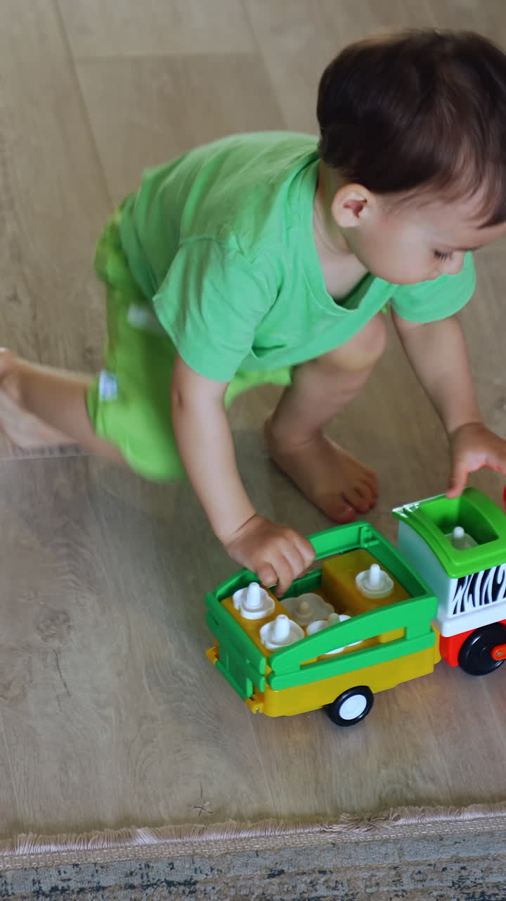 Caucasian toddler puts his toy car on batteries on the side. Kid watches how the wheels move. Top view. Vertical video