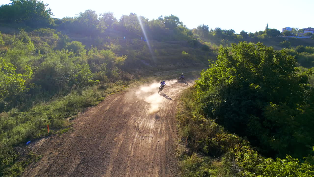 Vista aerea da drone di motociclisti che saltano da trampolini durante una gara di motocross, pista fangosa, rally di moto, vegetazione circostante
