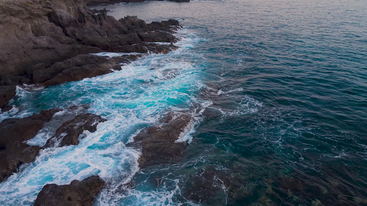 Waves crash on Costa Alcala's rocky shore in Tenerife at sunset