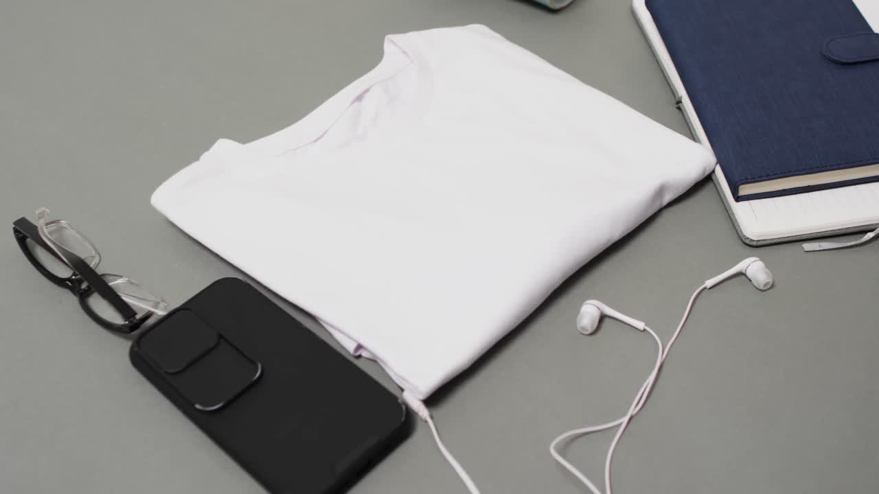 Video of white t shirt, smartphone and earphones with copy space on grey background