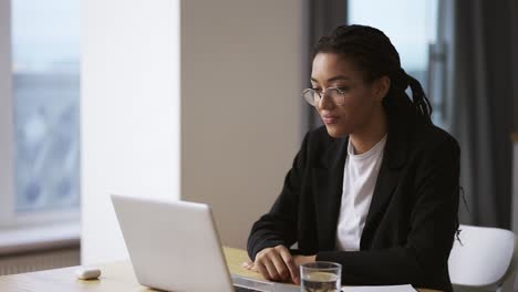 afro american girl secretary business woman sitting at table at office using laptop, slow motion