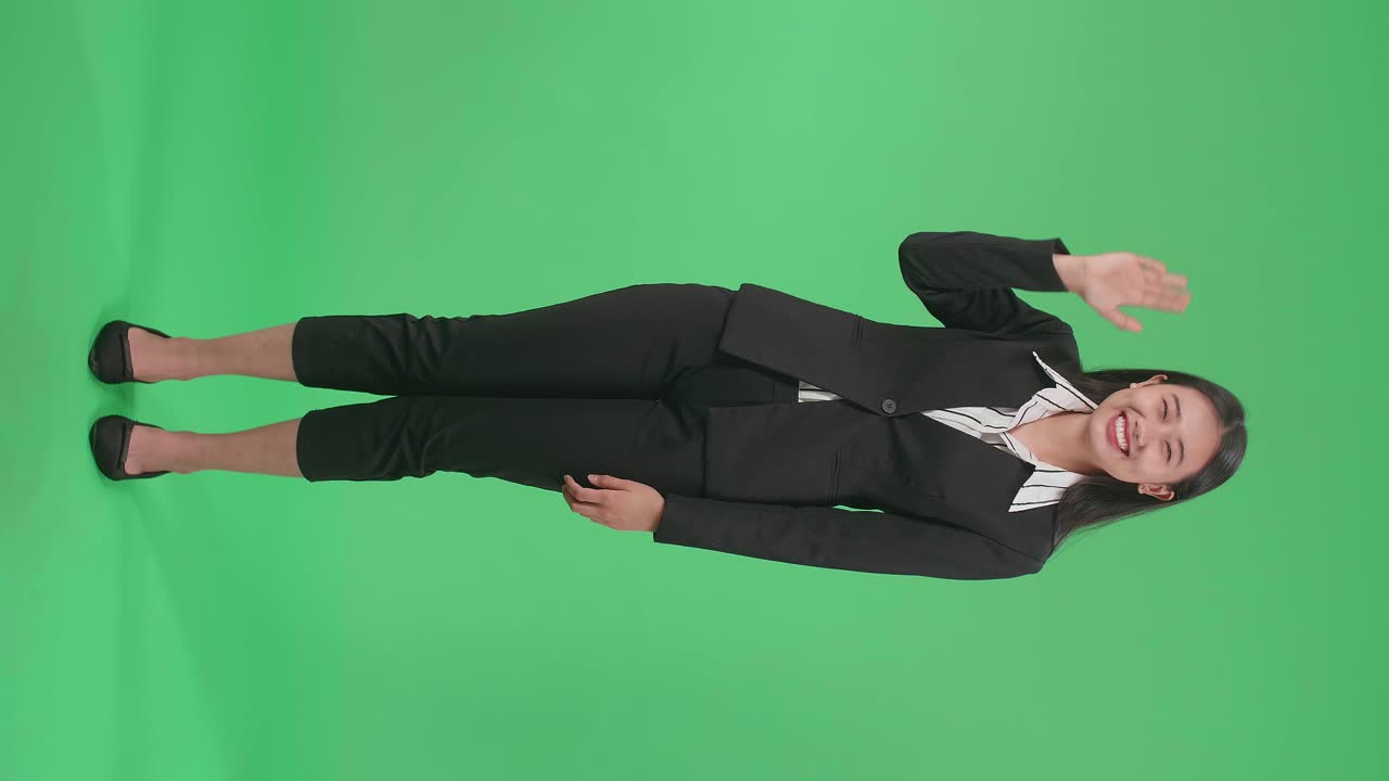Full Body Of An Asian Business Woman Waving Hand And Smiling While Standing On Green Screen In The Studio