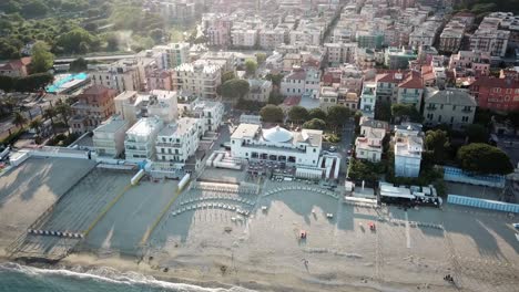 Drone,-sunset-panning-shot-of-a-town-next-to-the-Mediterranean-shore-with-sandy-beach