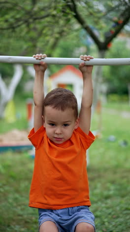 cute baby boy hanging on the horizontal bar. barefoot child tries to tumble on the sport inventory in the garden. vertical video.