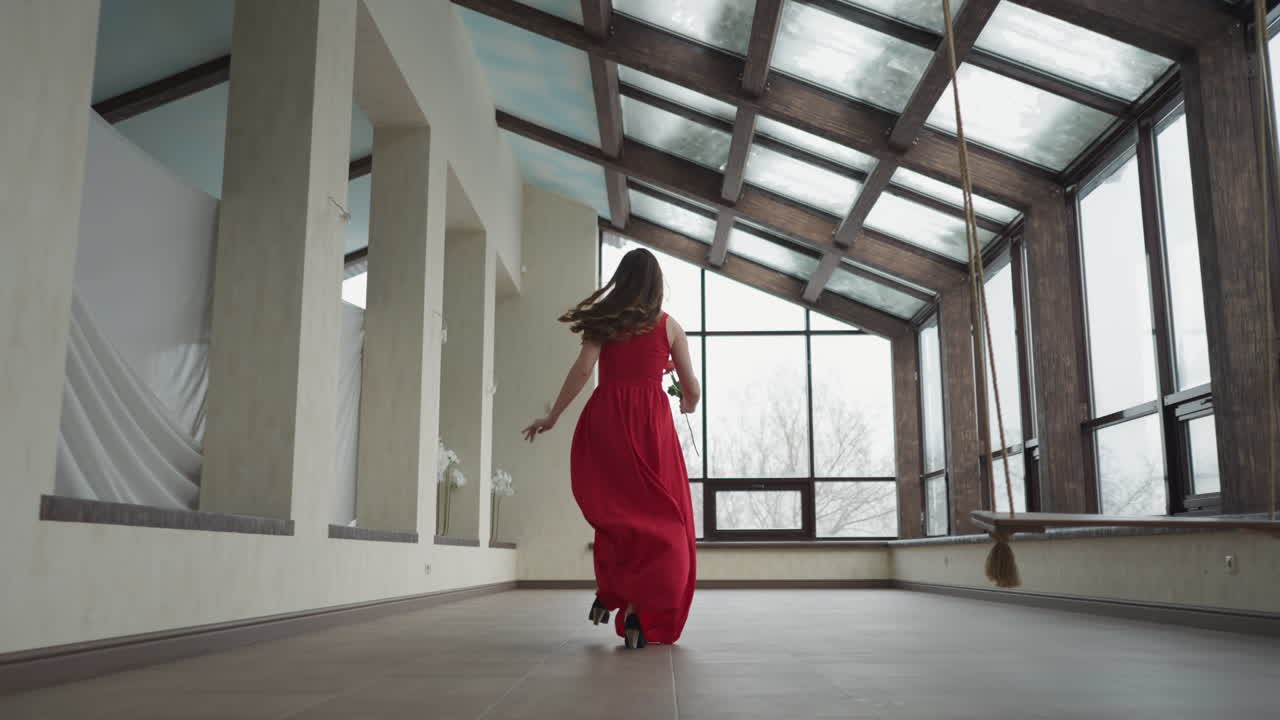 Una modella in abito svolazzante si avvicina rapidamente alla finestra. La giovane donna crea un momento visivamente accattivante in movimento in una galleria d'arte. Un contrasto sorprendente con l'ambiente circostante.