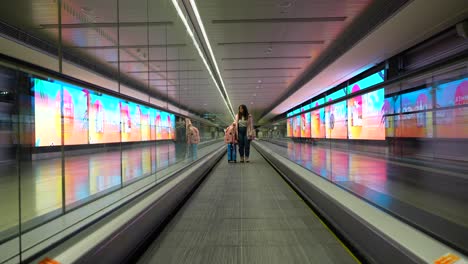 Woman-moving-in-international-airport-automatic-belt-with-her-luggage-with-led-panels-around