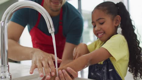 Happy-biracial-father-and-daughter-washing-hands-in-kitchen