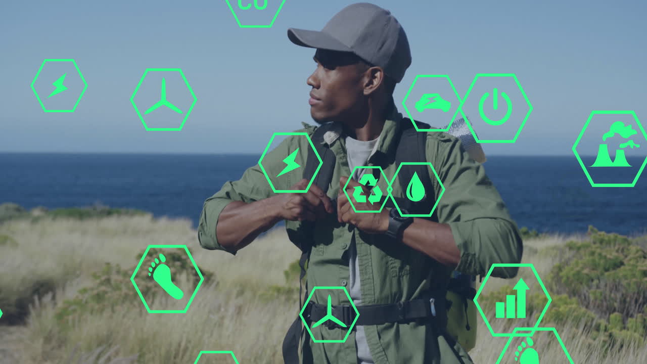 man adjusting backpack on coastal bluff, showing green hexagon icons tracking renewable energy data