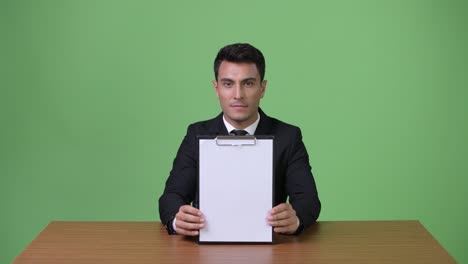 young handsome hispanic businessman against green background