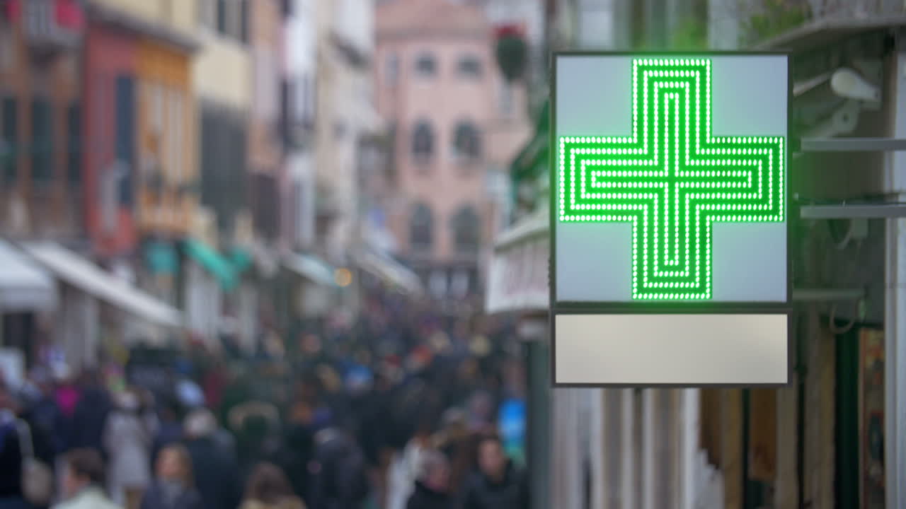 un letrero de farmacia con una cruz verde en una calle concurrida