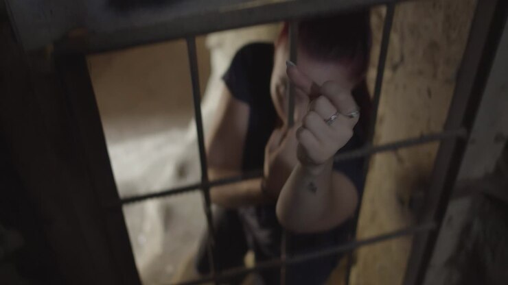 A young woman stretches out her hand through the bars trapped in an old, abandoned building