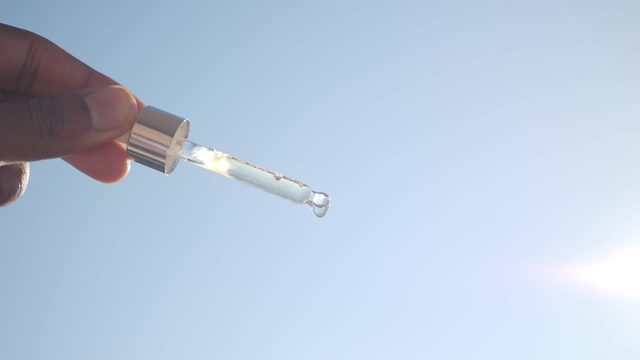 Hand holding a dropper bottle with liquid against a clear blue sky