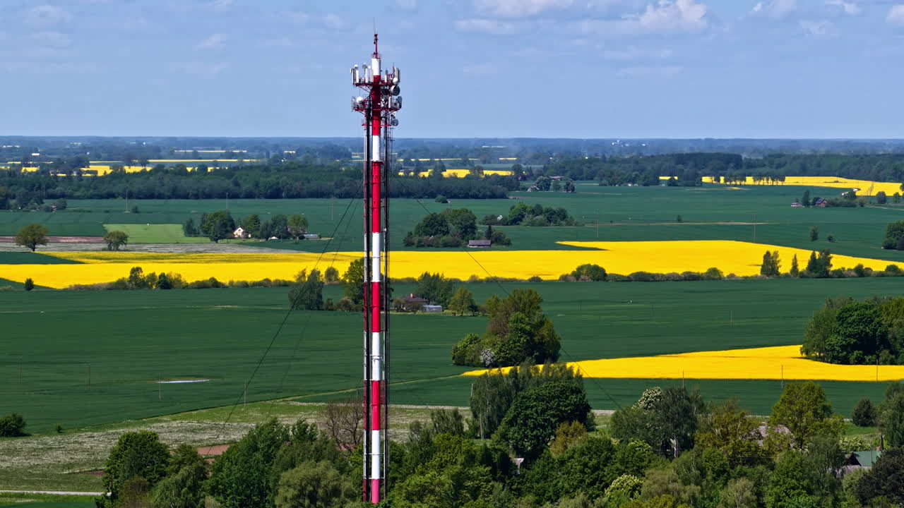 Droe video of communication tower rising above rapeseed and green fields