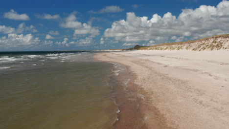 Rückwärts-Fliegen-über-Milde-Wellen,-Die-Sandstrand-An-Der-Küste-Waschen.-Sonniger-Tag-In-Jütland.-Blauer-Himmel-Mit-Weißen-Wolken.-Dänemark