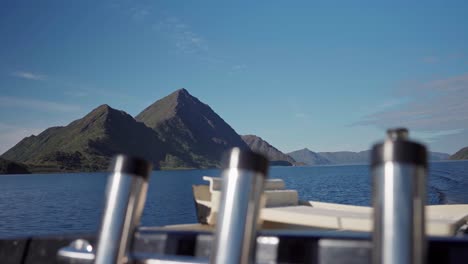 fishing rod holder of a traveling boat with mountains in background during sunny day in norway